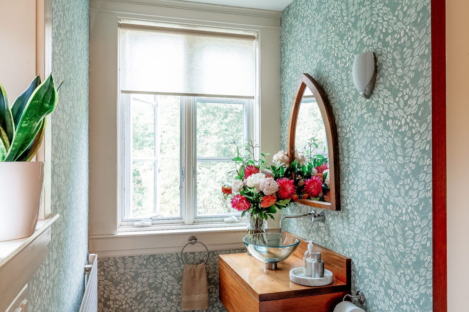 A bathroom with a mirror and flowers in the corner.