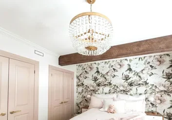 A bedroom with a bed, chandelier and floral wallpaper.